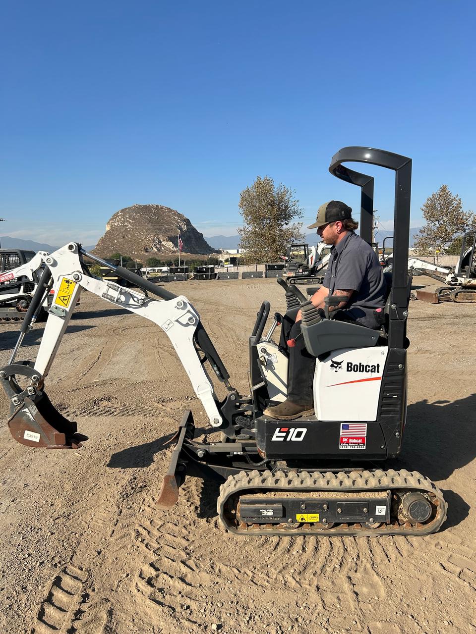 worker operating a compact mini excavator digging into dirt at a construction or landscaping site.