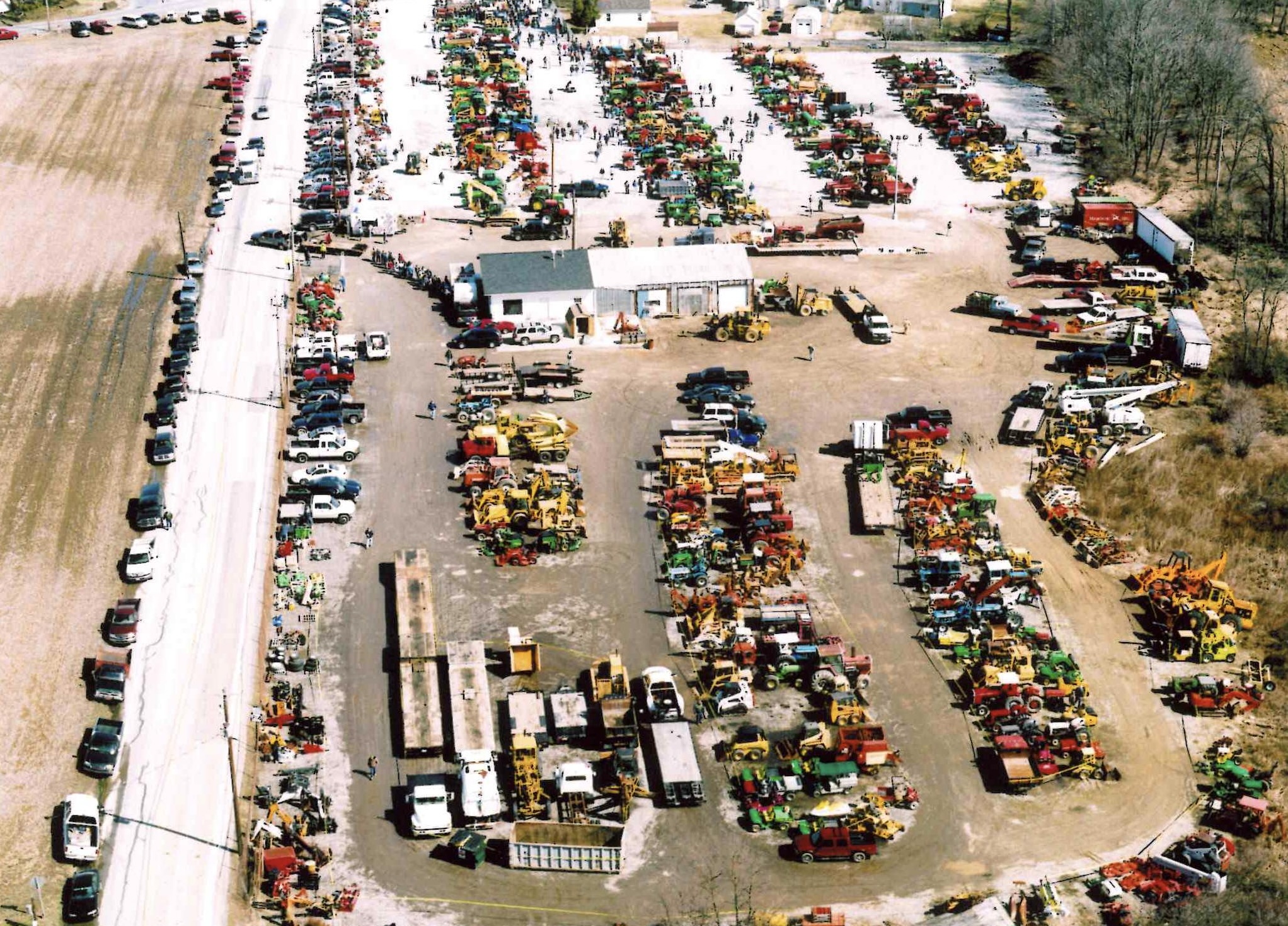 high-angle aerial shot of a large outdoor auction yard filled with organized rows of construction and farm equipment.