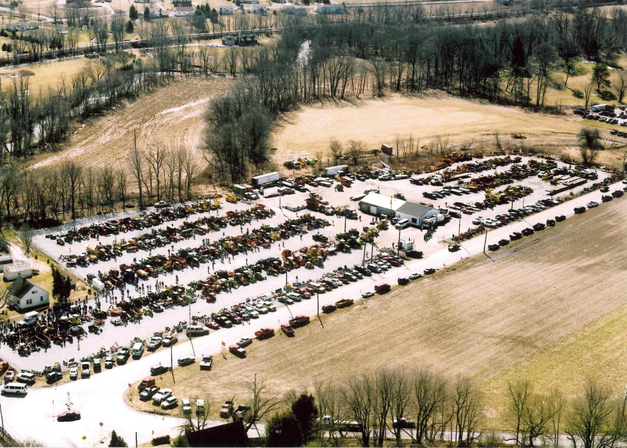 Aerial view of a large equipment auction yard with rows of parked heavy machinery arranged across open fields