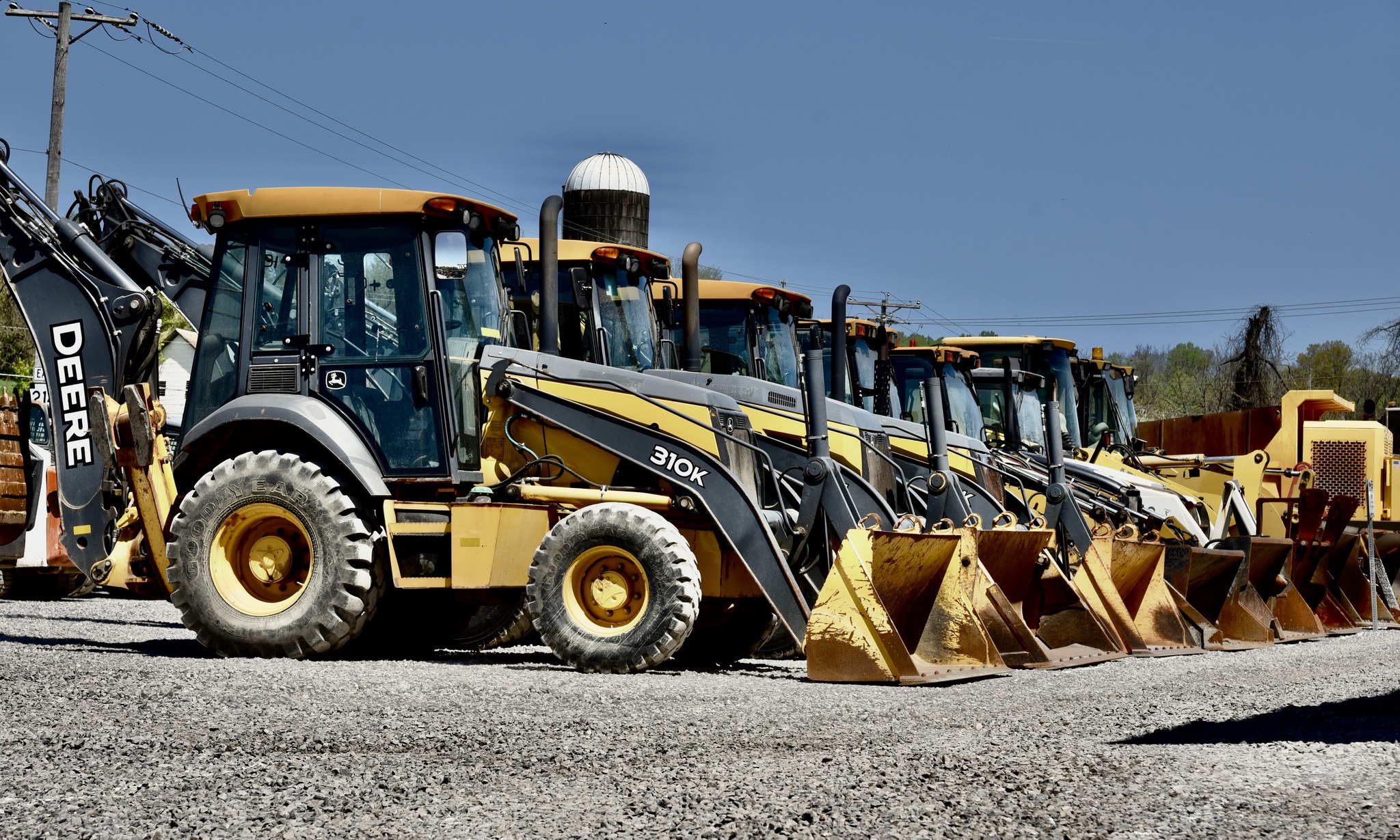 Front view of a row of wheel loaders lined up on gravel, showing buckets 