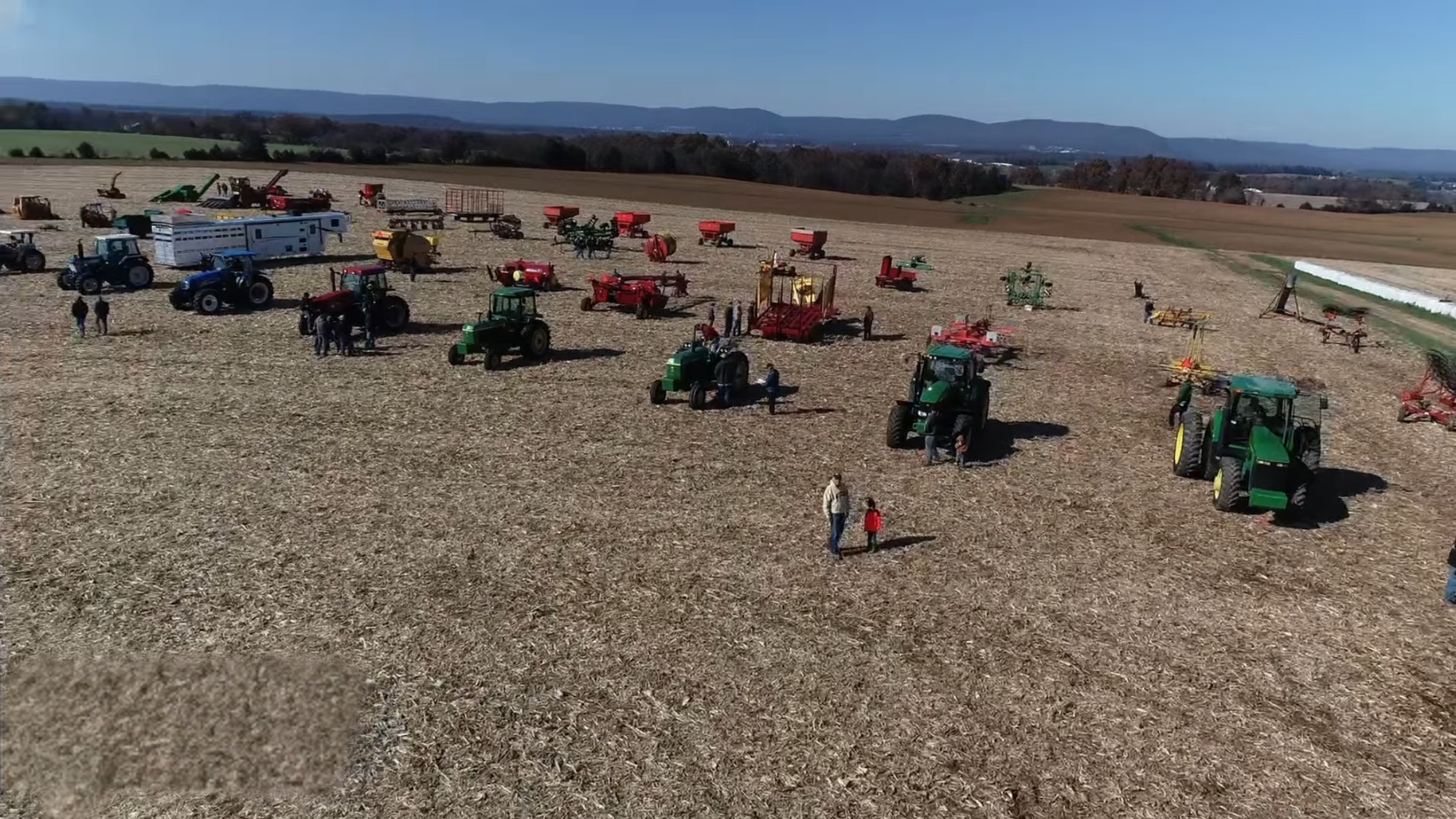 wide shot of various tractors and farm machinery parked in a large open field