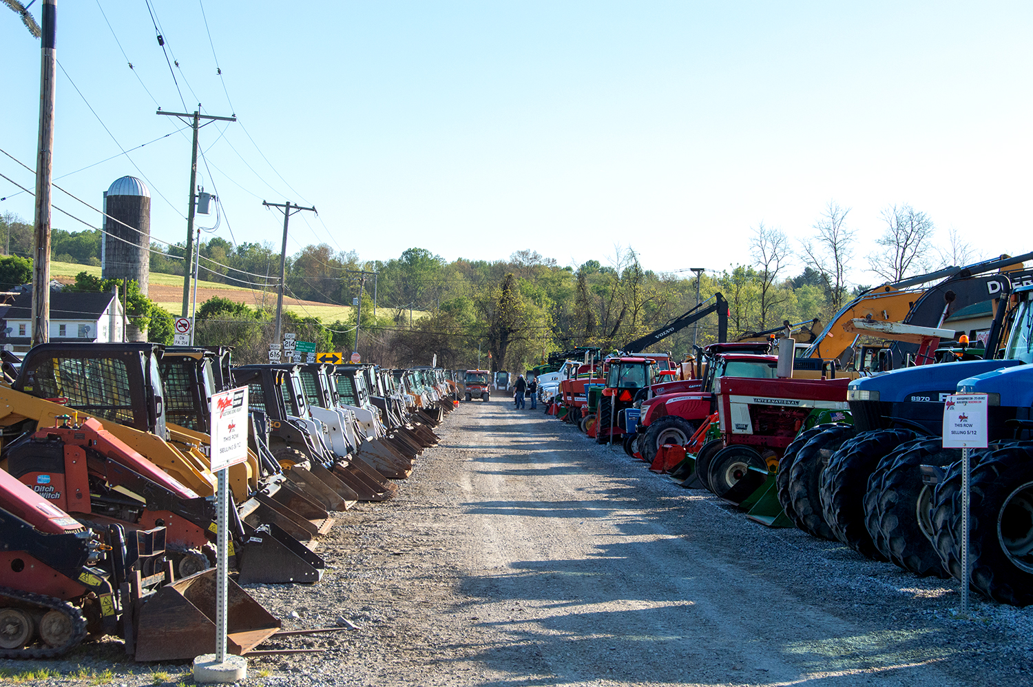 Looking Down Auction Lot Row of Skid Steers on the left and Tractors on the right